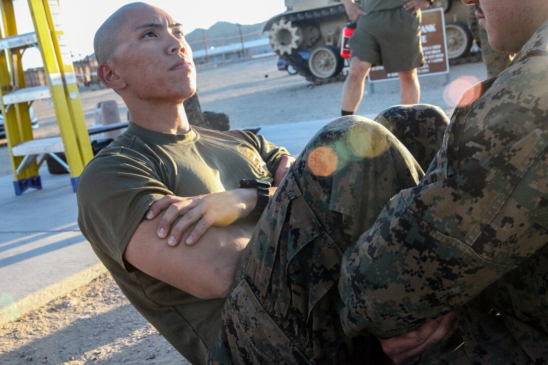 Sgt. Riordan T. Anunciacion, an intelligence specialist with Headquarters Company, 23rd Marine Regiment, 4th Marine Division, based in San Bruno, California, demonstrates correct form for crunches while monitoring a physical fitness test during Integrated Training Exercise 4-18 at Marine Corps Air Ground Combat Center Twentynine Palms, California, on June 24, 2018. Monitoring PFTs is one of many responsibilities Anunciacion has taken on that led him to win the 23rd Marines Noncommissioned Officer of the Quarter award. (United States Marine Corps photo by Cpl. Alexis B. Rocha/released)