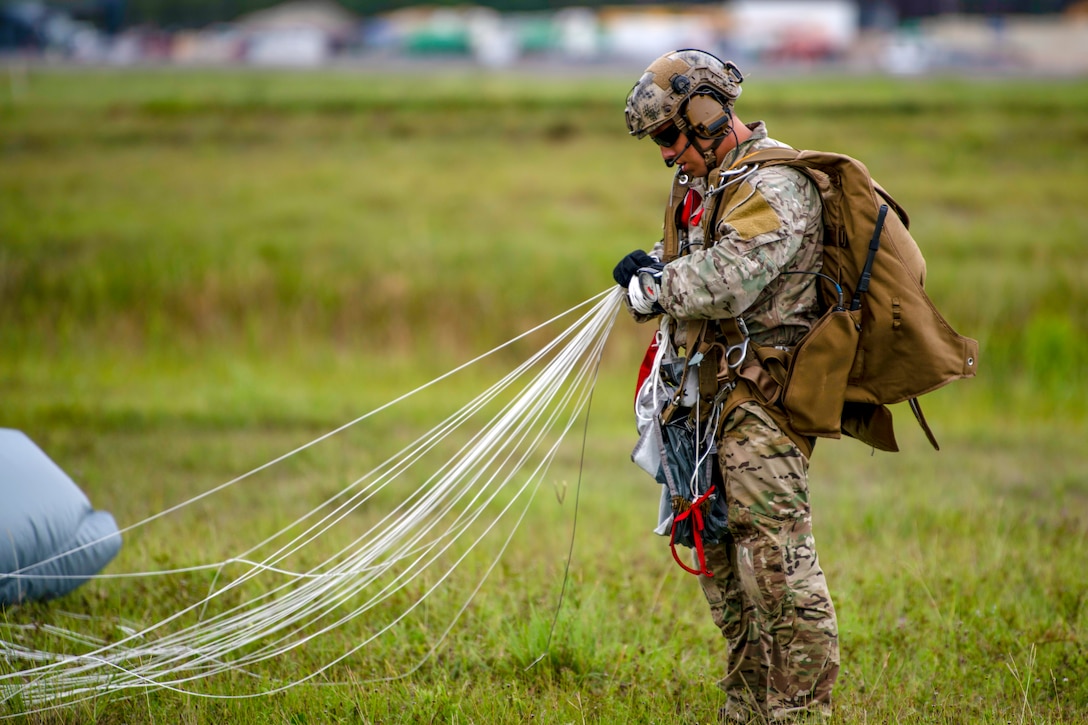 An airman stands on the ground and holds the lines of a parachute.