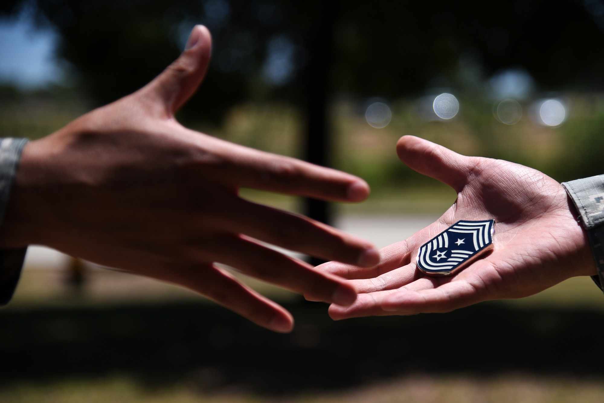 A challenge coin passes from one person to another near building 533 on Goodfellow Air Force Base, Texas, June 28, 2018. A challenge coin signifies inclusion to a group or can be given out as small tokens of appreciation. (U.S. Air Force photo by Staff Sgt. Joshua Edwards/Released)