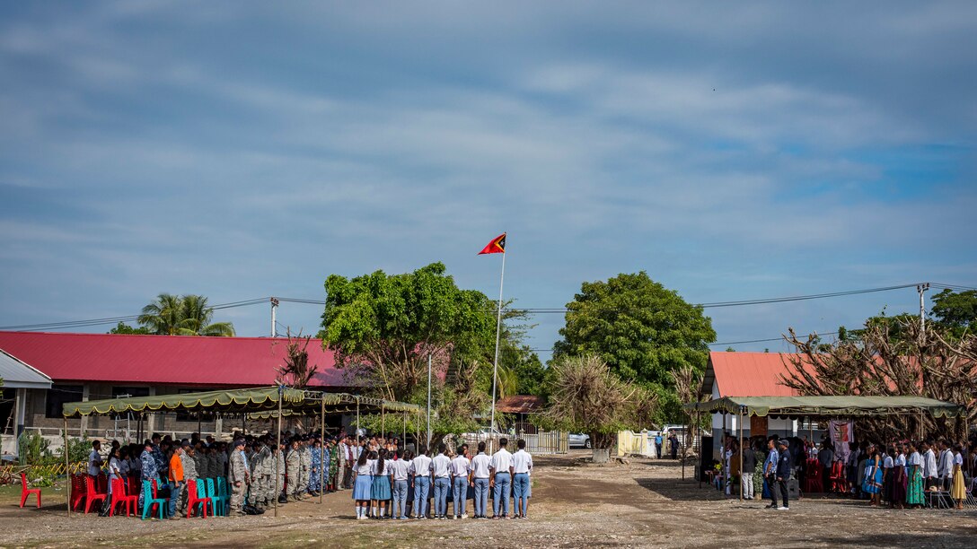 Attendees stand for the playing of the Timor-Leste national anthem during the closing ceremonies of Pacific Angel (PAC ANGEL) 2018 at the Negri Saran Kote Secondary School in Suai, Cova Lima Municipality, Southwest Timor-Leste, June 18, 2018.