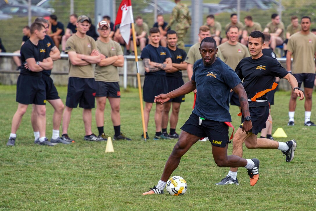 Soldier kick a soccer ball while being watched by other soldiers.