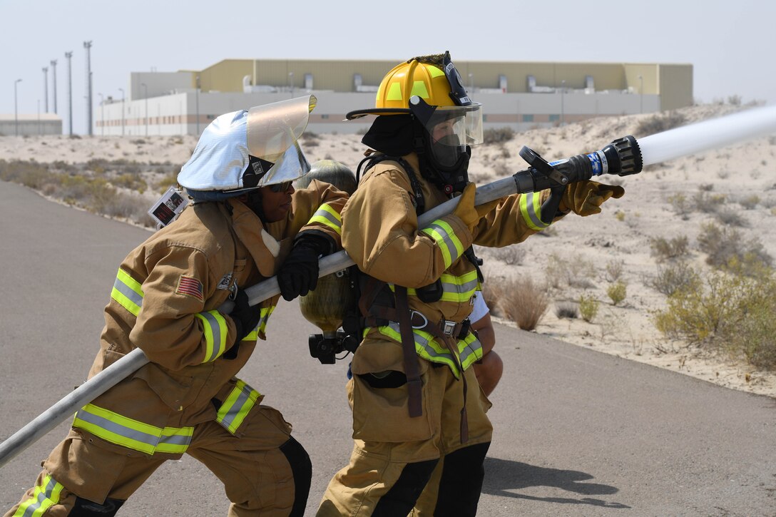 Senior Airman Rachel Johnson, 380th Civil Engineering Squadron emergency manager, and Staff Sgt. Staff Sgt. Jamie Perkins, 380th ECES firefighter, spray an open area with a fire hose during a ‘Firefighter for a Day’ training at Al Dhafra Air Base, June 25. This exercise demonstrated to Johnson, the ‘Firefighter for a Day’ the force that comes from a high pressure water hose and the strength needed to properly hold it. (U.S. Air Force photo by Staff Sgt. Erica Rodriguez)