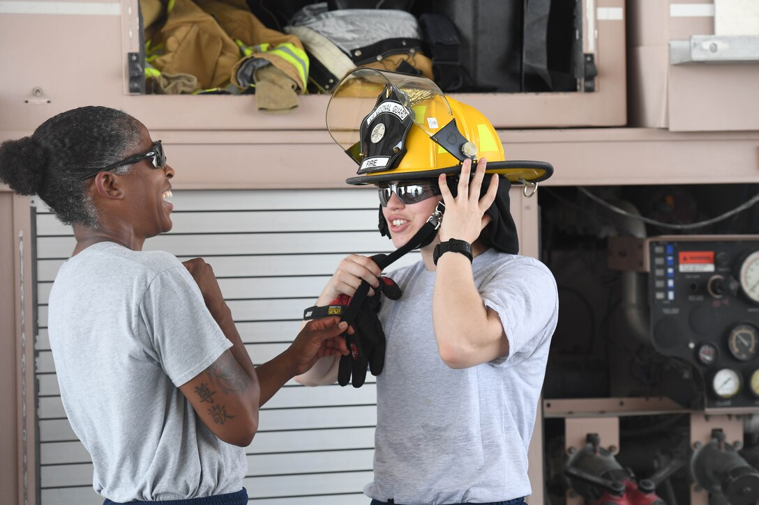 Senior Airman Rachel Johnson, 380th Civil Engineering Squadron emergency manager, puts on fire protective gear with the help of Staff Sgt. Staff Sgt. Jamie Perkins, 380th ECES firefighter, during her ‘Firefighter for a Day’ training at Al Dhafra Air Base, June 25.  (U.S. Air Force photo by Staff Sgt. Erica Rodriguez)