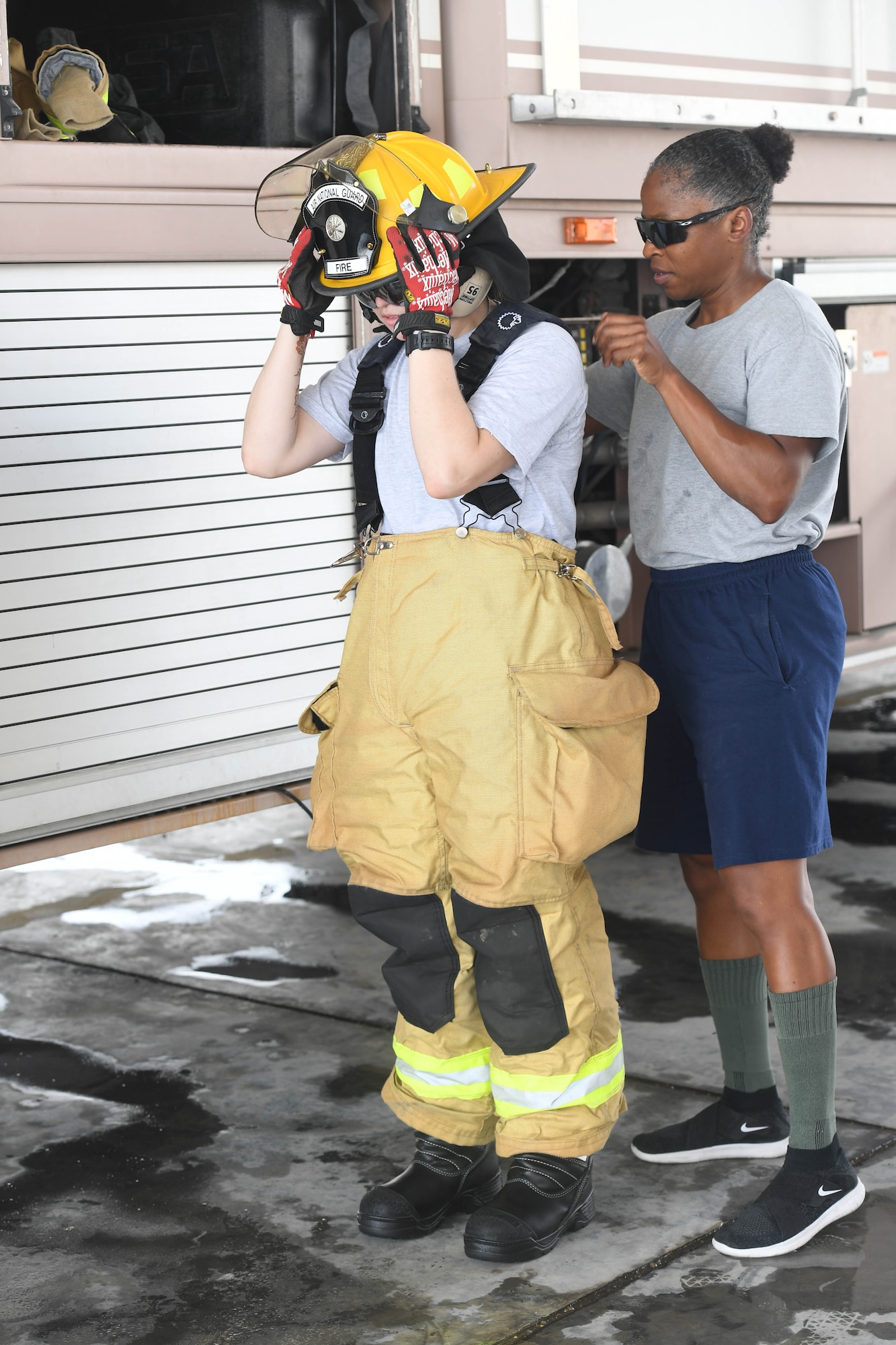 Senior Airman Rachel Johnson, 380th Civil Engineering Squadron emergency manager, puts on fire protective gear with the help of Staff Sgt. Staff Sgt. Jamie Perkins, 380th ECES firefighter, during her ‘Firefighter for a Day’ training at Al Dhafra Air Base, June 25.  (U.S. Air Force photo by Staff Sgt. Erica Rodriguez)