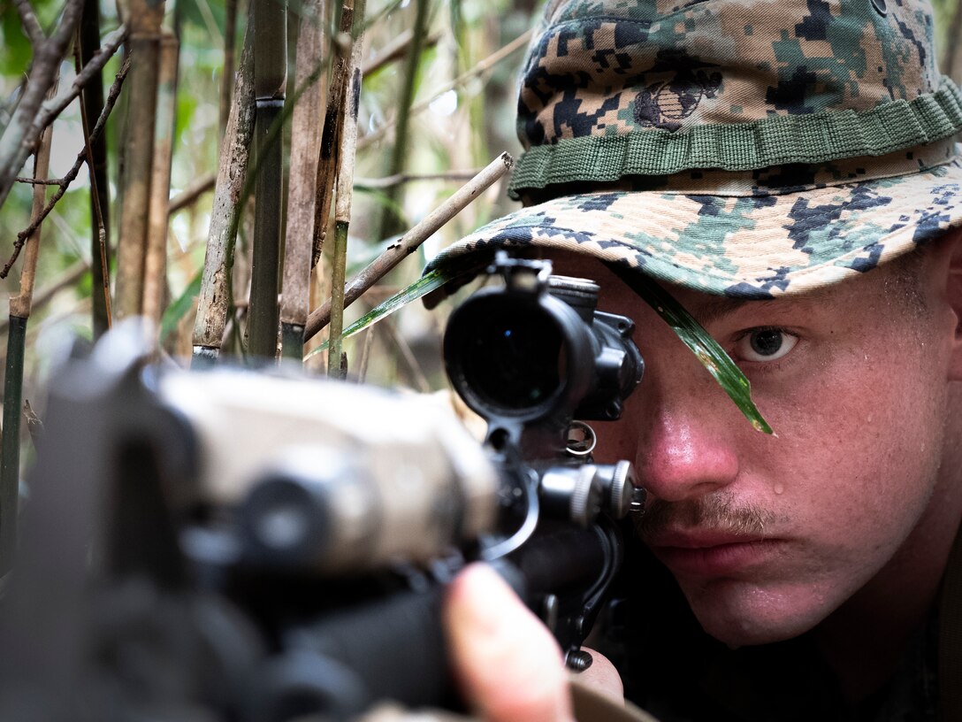 A Marine with Headquarters Company, Headquarters Battalion, 3rd Marine Division, sights in while posting 360 degree security during a patrol at the Jungle Warfare Training Center, Camp Gonsalves, Okinawa, Japan June 28, 2018. The Marines are participating in a one week course to improve their jungle survival skills.