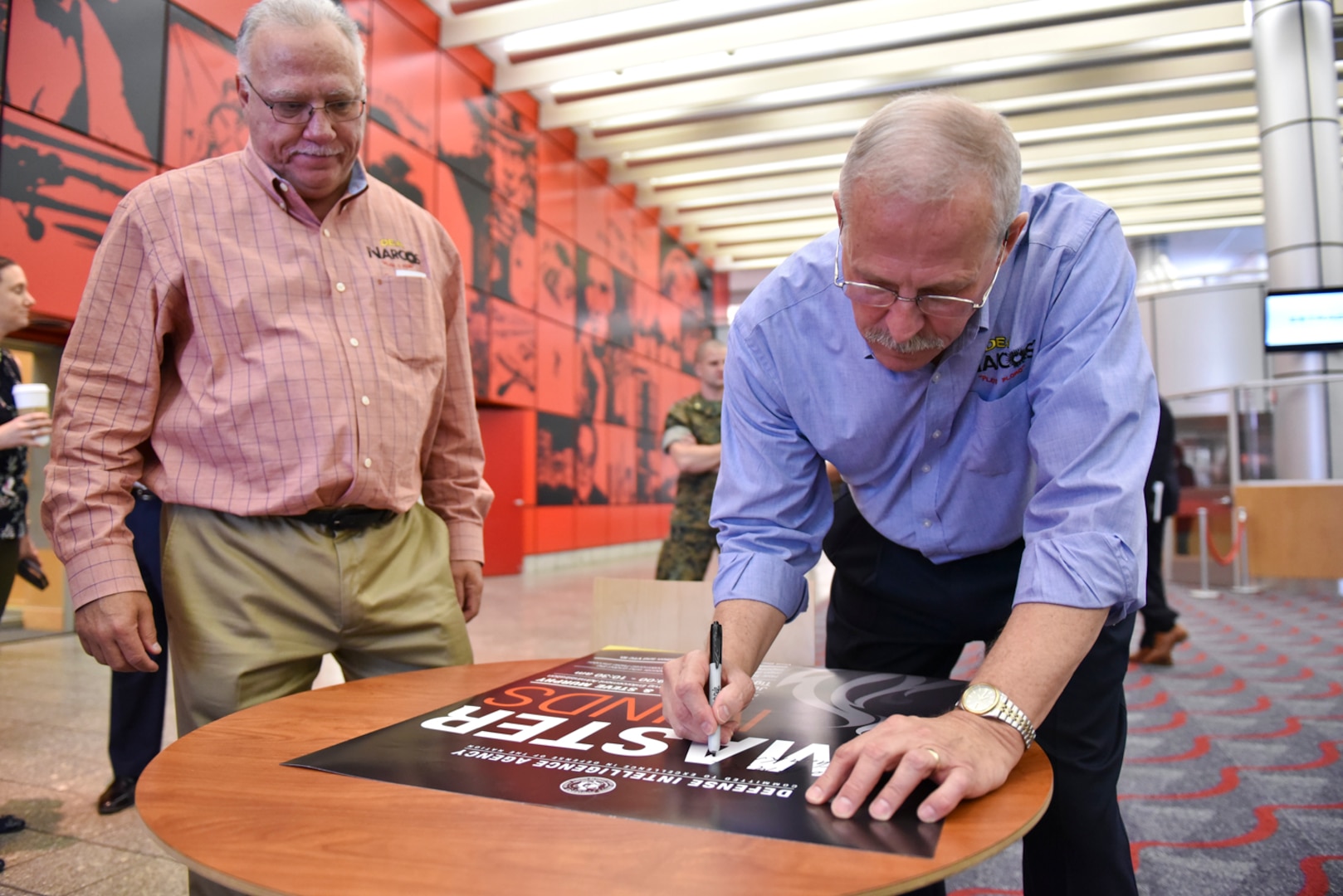 Steve Murphy, right, and Javier Peña autograph a poster at the conclusion of their visit to the Defense Intelligence Agency headquarters, June 21.