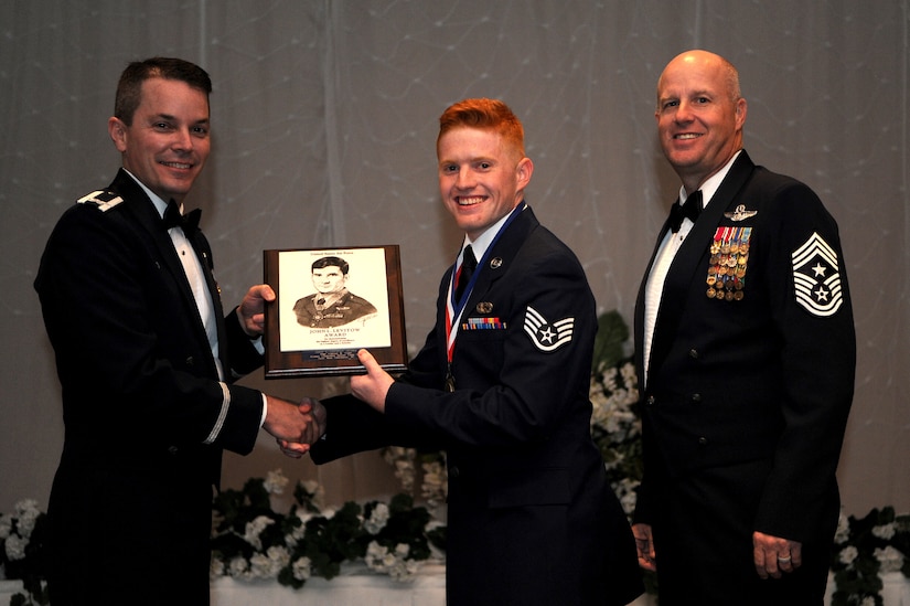 Col. Jeffrey Nelson, left, 628th Air Base Wing commander, and Chief Master Sgt. Todd Cole, right, 628th Air Base Wing command chief, present Staff Sgt. Clayton Cupit, 1st Combat Camera Squadron, a plaque for earning the John L. Levitow Award during the class 18-E Airman Leadership School Graduation at the Charleston Club here June 29, 2018.