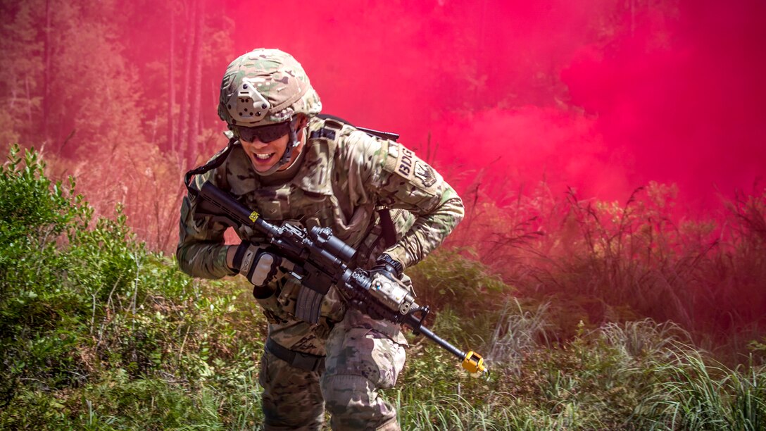 An airman carrying a weapon runs ahead of magenta smoke.