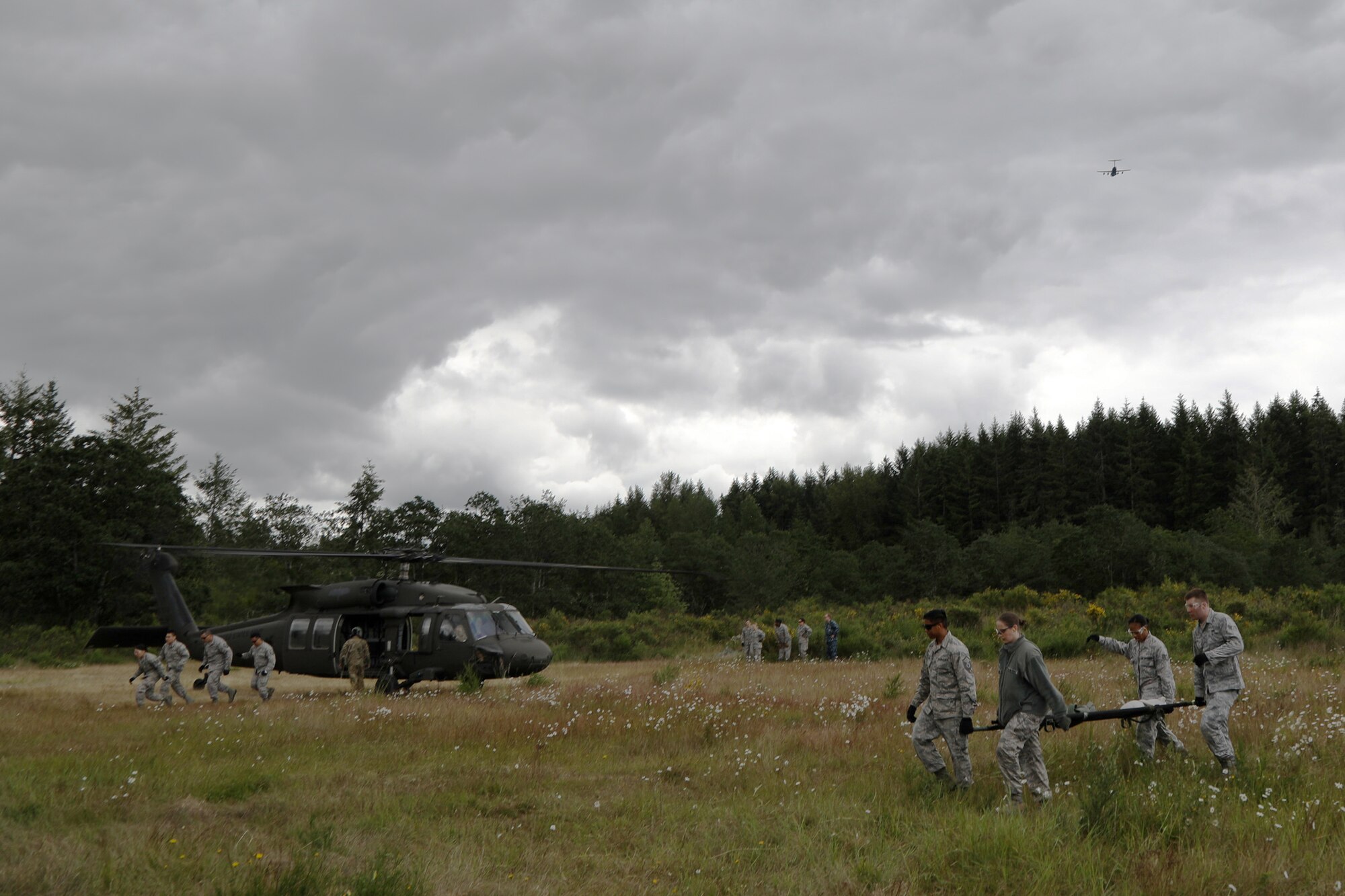 A C-17 Globemaster III flies over Air Force and Navy Reserve medics as they take part in Rainier Medic, June 13, 2018, on Joint Base Lewis-McChord, Wash. Rainier Medic is a combined training event meant to sharpen skills often used in joint mission accomplishment. (U.S. Air Force photo by David L. Yost)