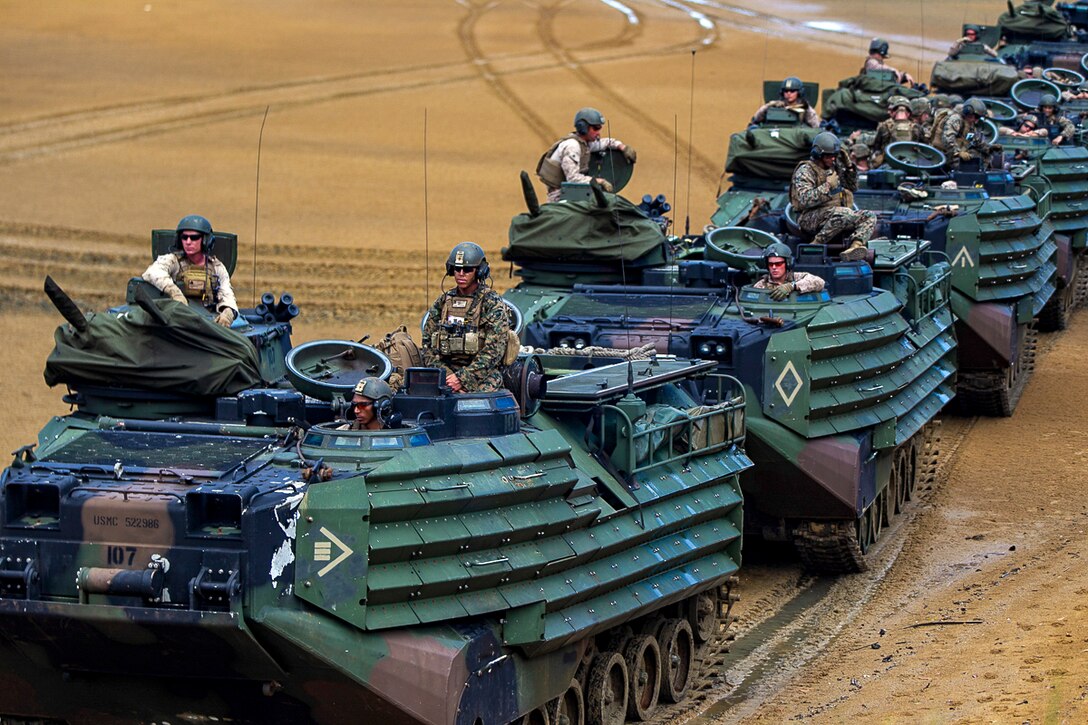 Marines sit in amphibious vehicles on a beach.