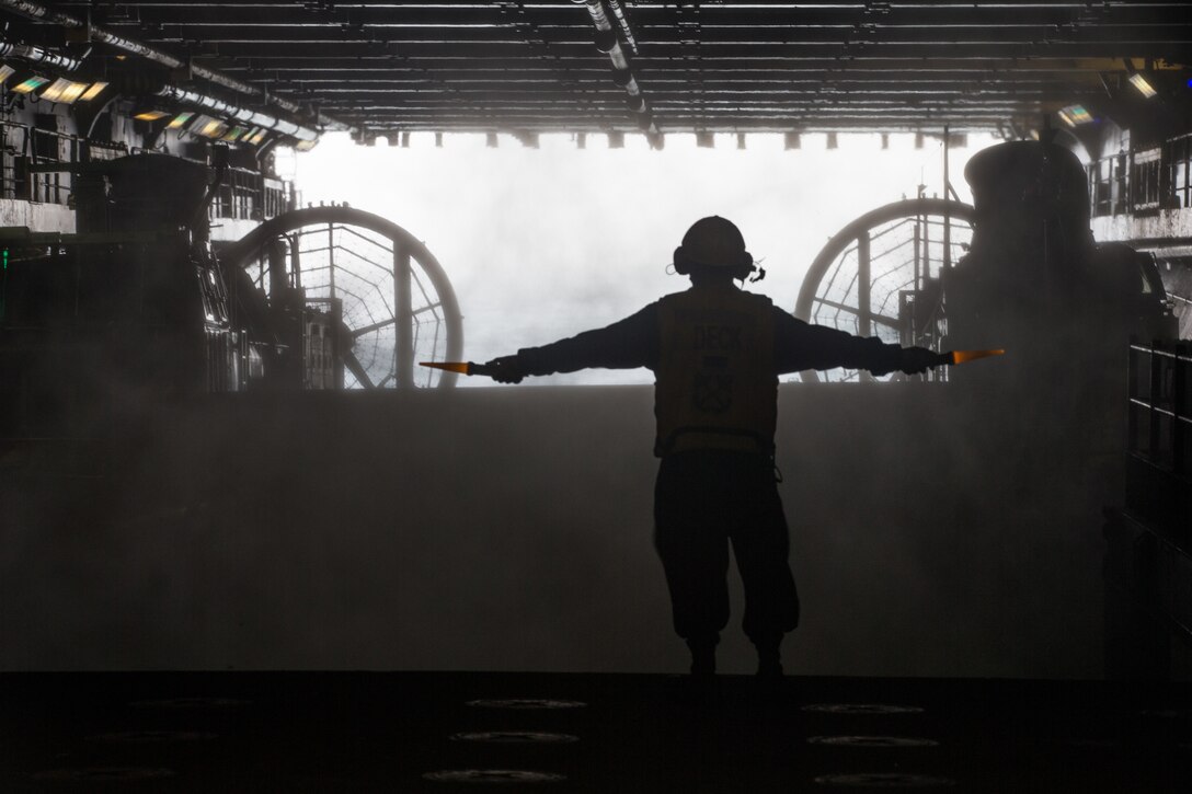 A U.S. Navy Sailor with the Iwo Jima Amphibious Ready Group (ARG), signals a Landing Craft Air Cushion (LCAC) to depart the well deck of the amphibious assault ship USS Iwo Jima (LHD 7), Feb. 11, 2018.