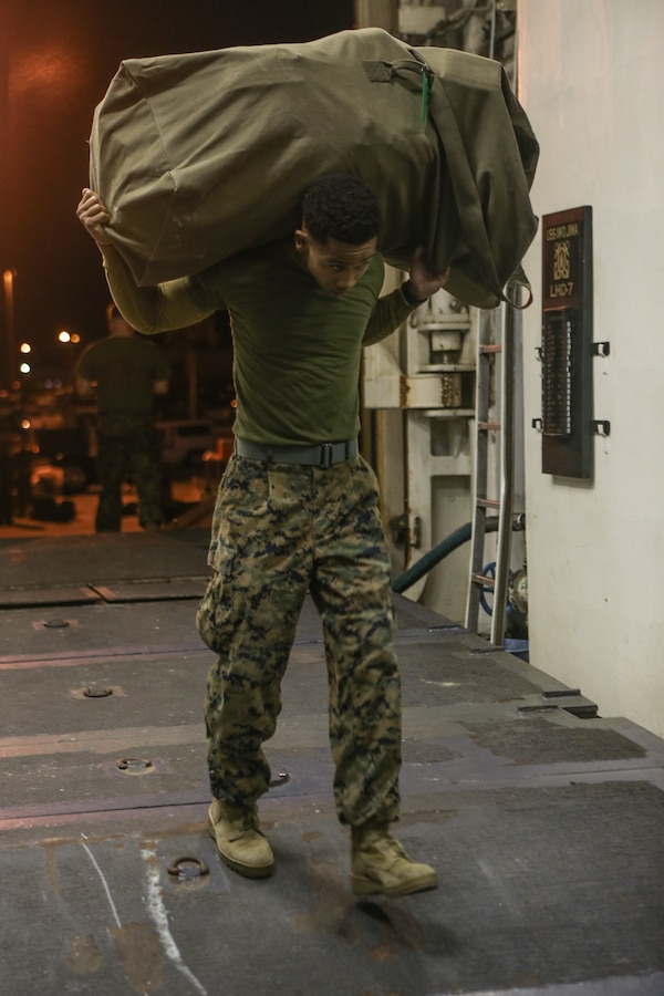 A U.S. Marine with the 26th Marine Expeditionary Unit (MEU), carries his gear onboard the amphibious assault ship USS Iwo Jima (LHD 7) prior to deployment, Feb. 6, 2018. The 26th MEU is deploying at sea to conduct maritime security operations, crisis response and theater security cooperation, while also providing a forward expeditionary naval presence in Europe and the Middle East. (U.S. Marine Corps photo by Cpl. Jered T. Stone)