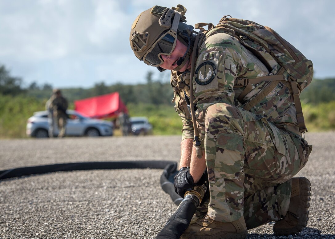 An airman connects hoses while setting up a helicopter expedient refueling system.