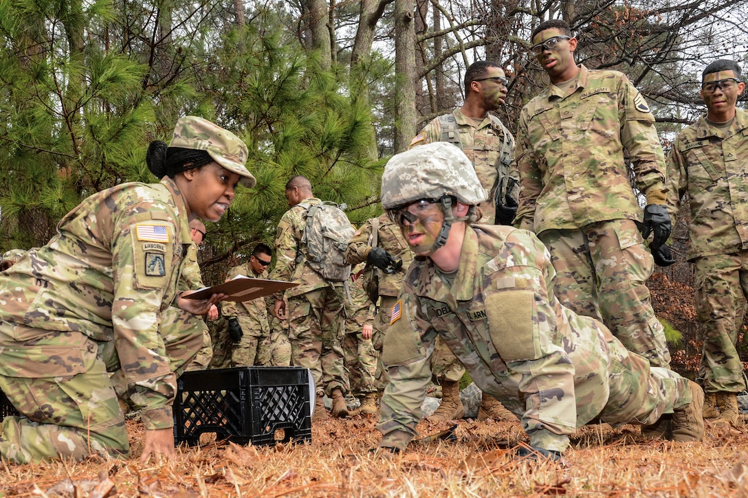 A soldier performs pushups during a competition as other soldiers look on.