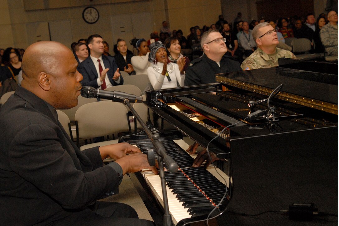 Key Arts Productions’ Joe Patterson (left foreground) plays piano and sings to accompany a video presentation of African-Americans in times of war at Defense Logistics Agency Troop Support in Philadelphia on Feb. 28.