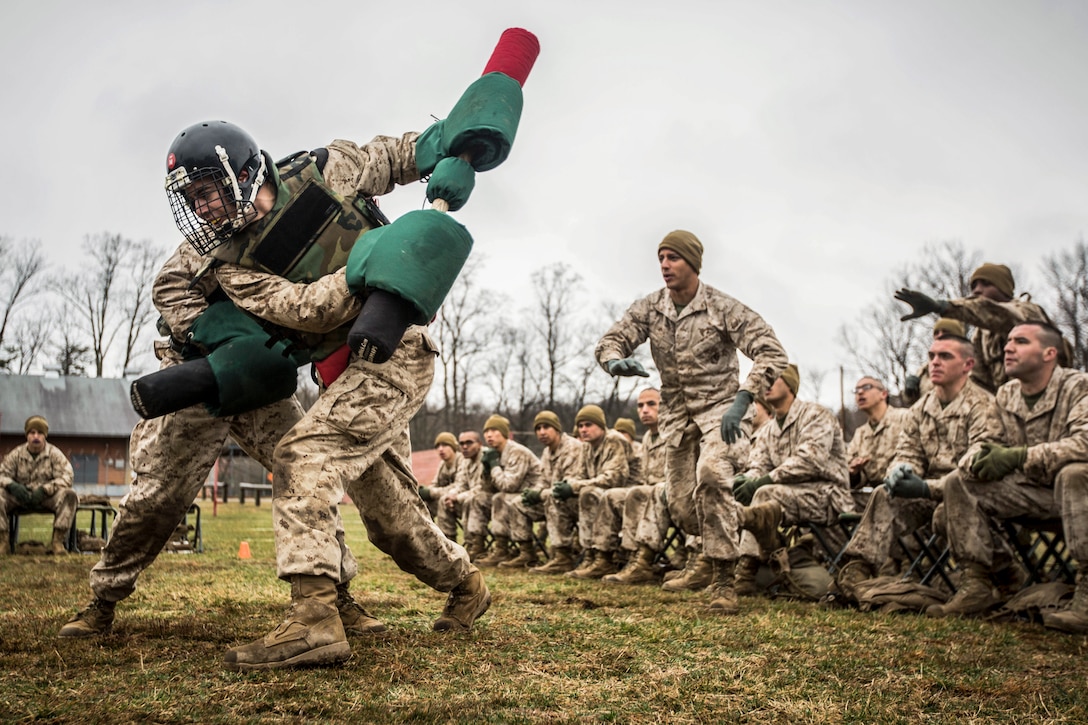 Marine officer candidates use pugil sticks during martial arts training as other Marines observe.