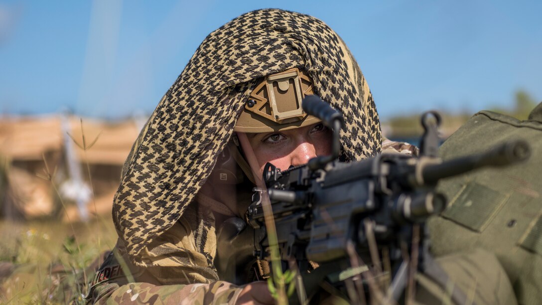 An airman lies in the grass as he aims a weapon.