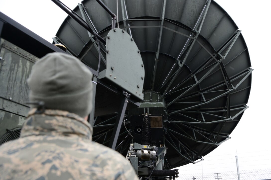An airman looks up at a large satellite antenna.
