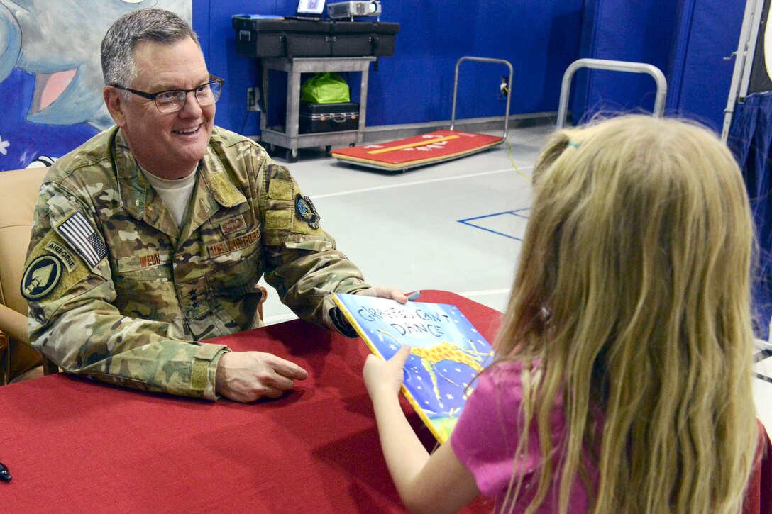 An Air Force officer hands a child a book.