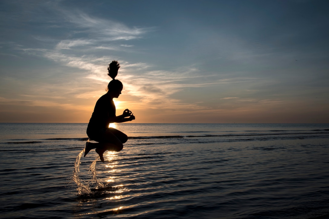A person jumps out of the water during sunrise.