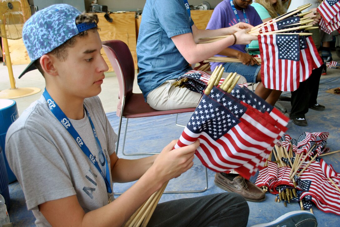 A civilian sits in a chair and rolls small American flags.