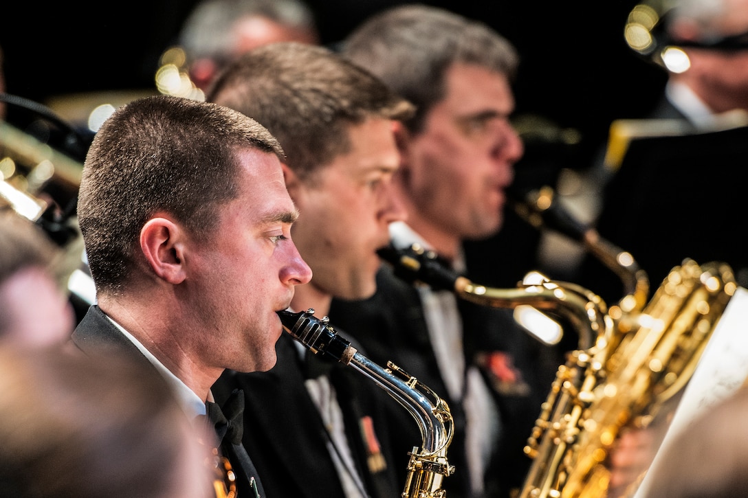 Three Navy musicians play in a band during a performance.