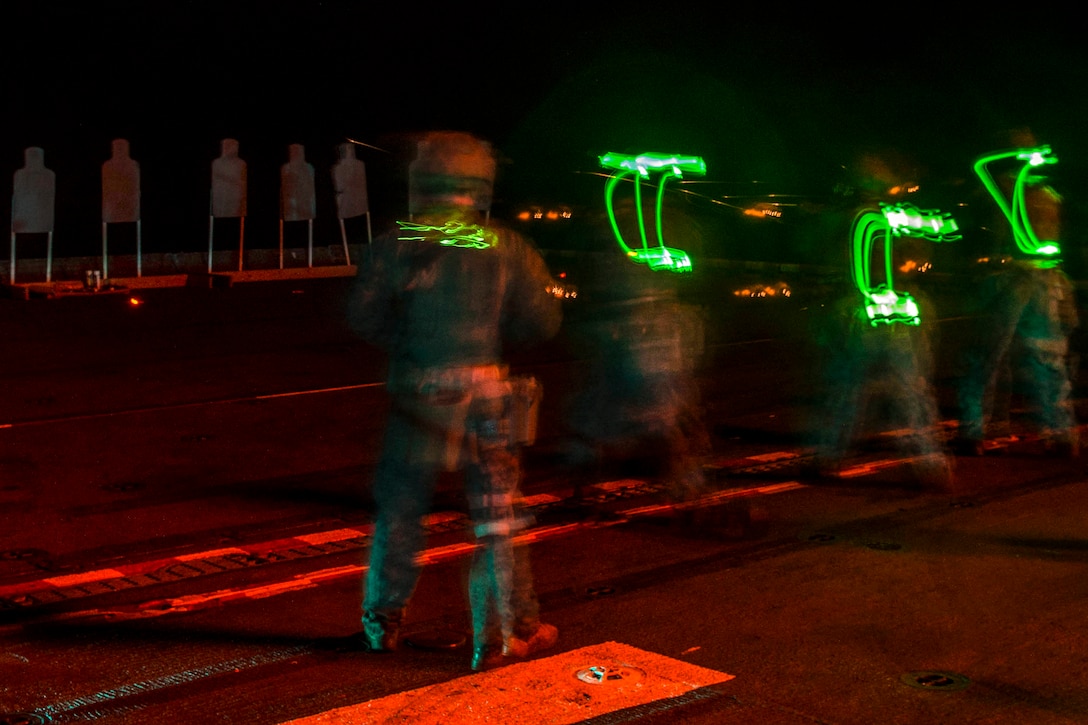 Marines participate in a small-arms gun shoot on a ship at night.