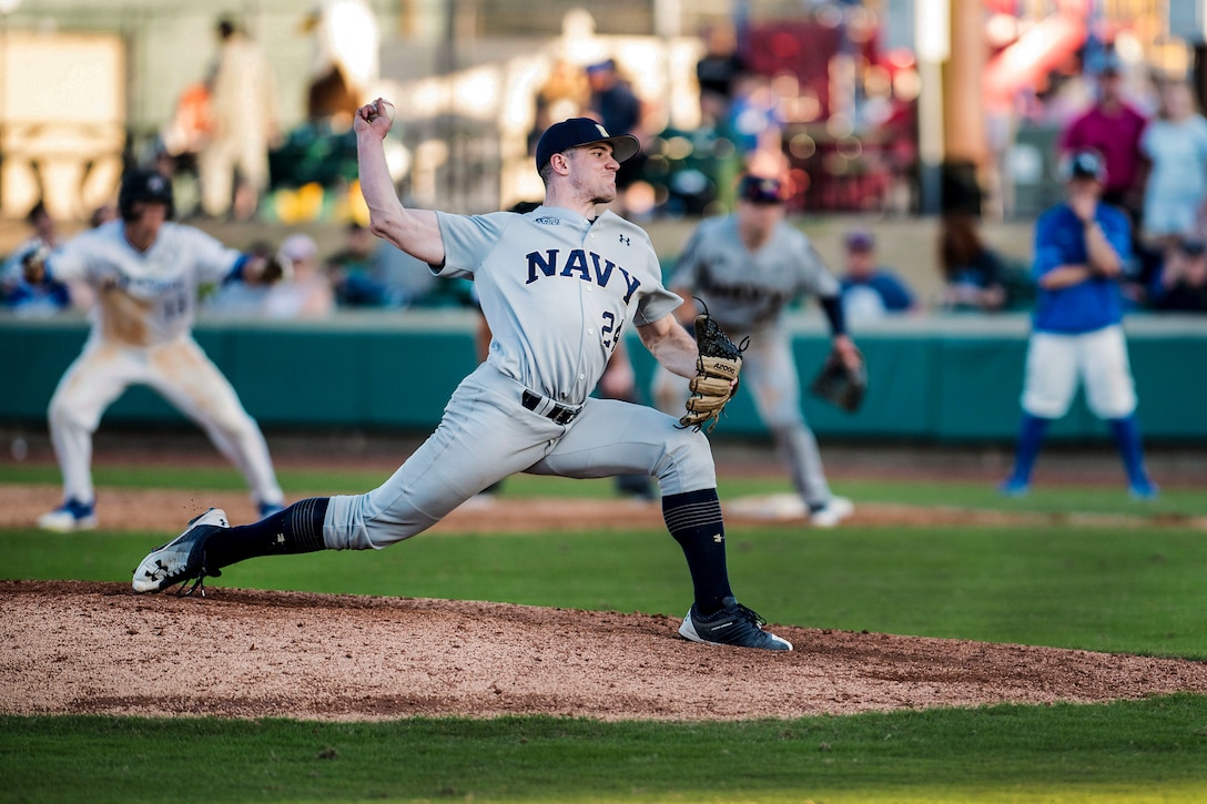 A pitcher holds his arm back and lunges forward on one knee before throwing a pitch on a baseball field.