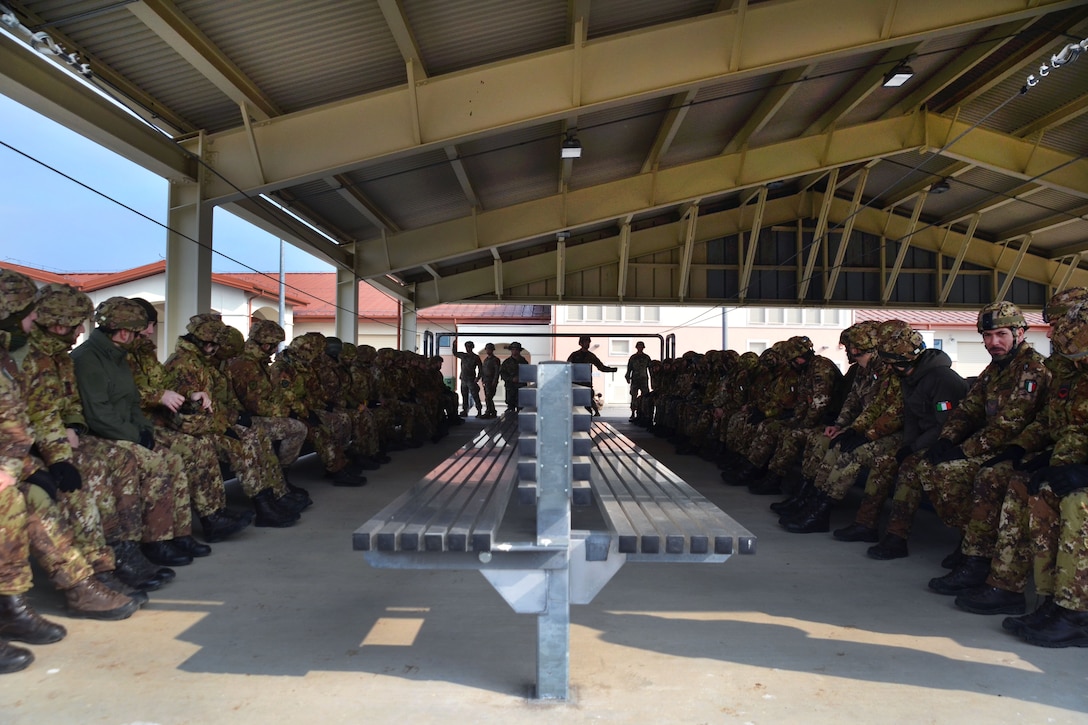 U.S. and Italian soldiers sit waiting for a jumpmaster to begin parachute landing fall training.