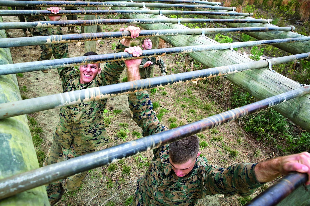 Marines work their way across bars of an obstacle.