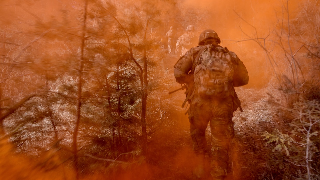 Soldiers run up a hill through orange smoke.