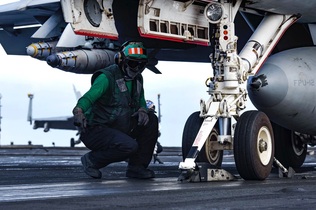 A sailor guides an F/A-18E Super Hornet aircraft onto a catapult.