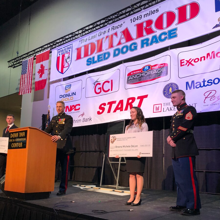 Maj. Brooks Boehlert, Commanding Officer, Recruiting Station Portland, presents two students with NROTC scholarship checks at the Iditarod Sled Dog Race Musher’s Banquet in Anchorage, Alaska. The Marine Corps partnered with the Iditarod for the first time, this year, to build a long-lasting connection and to demonstrate shared values such as honor, courage and commitment. (U.S. Marine Corps Photo by Capt. Maureen Krebs/Released)