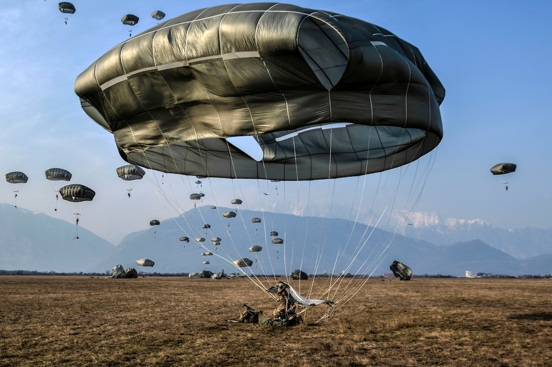 A paratrooper lands on the ground and the parachute deflates.