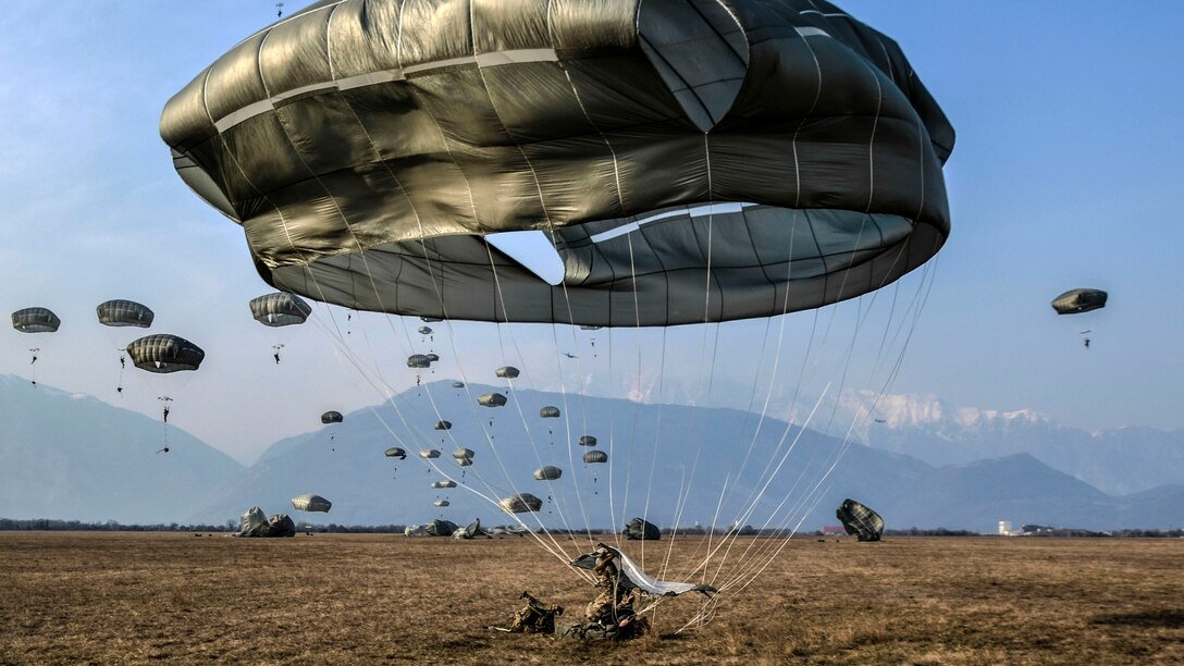 A paratrooper lands on the ground and the parachute deflates.