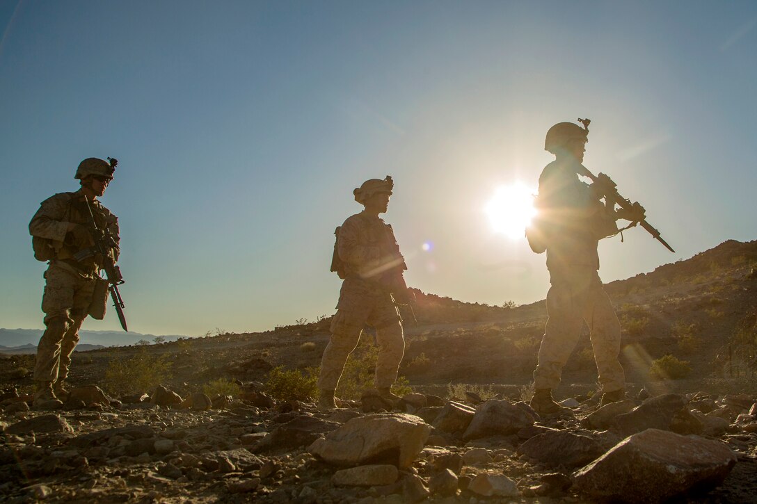 Four Marines walk across a ledge.