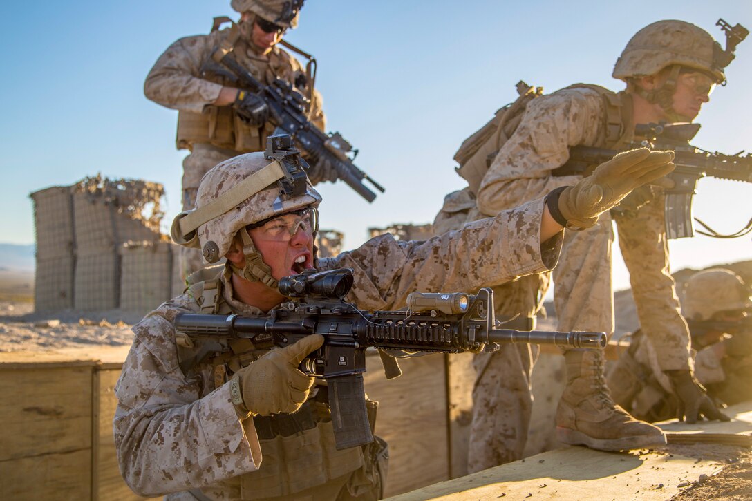 A Marine stretches out his arm and yells while other Marines move past.