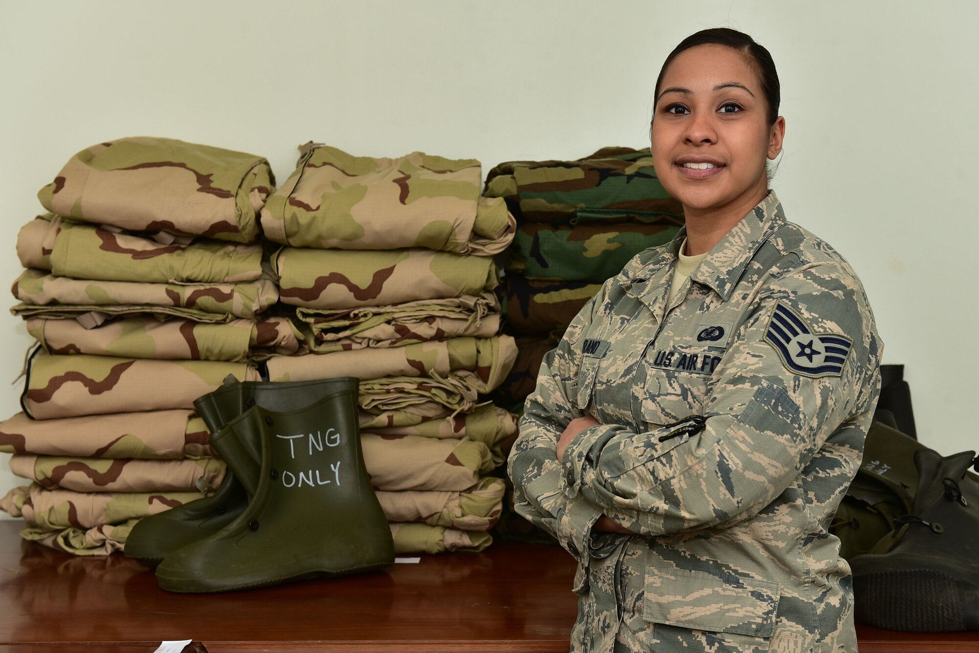 A woman stands in front of stacks of clothing.