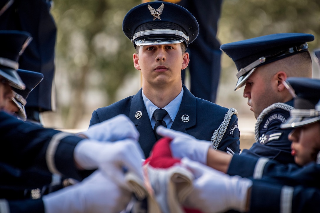 An airman watches as other airmen fold an American flag.