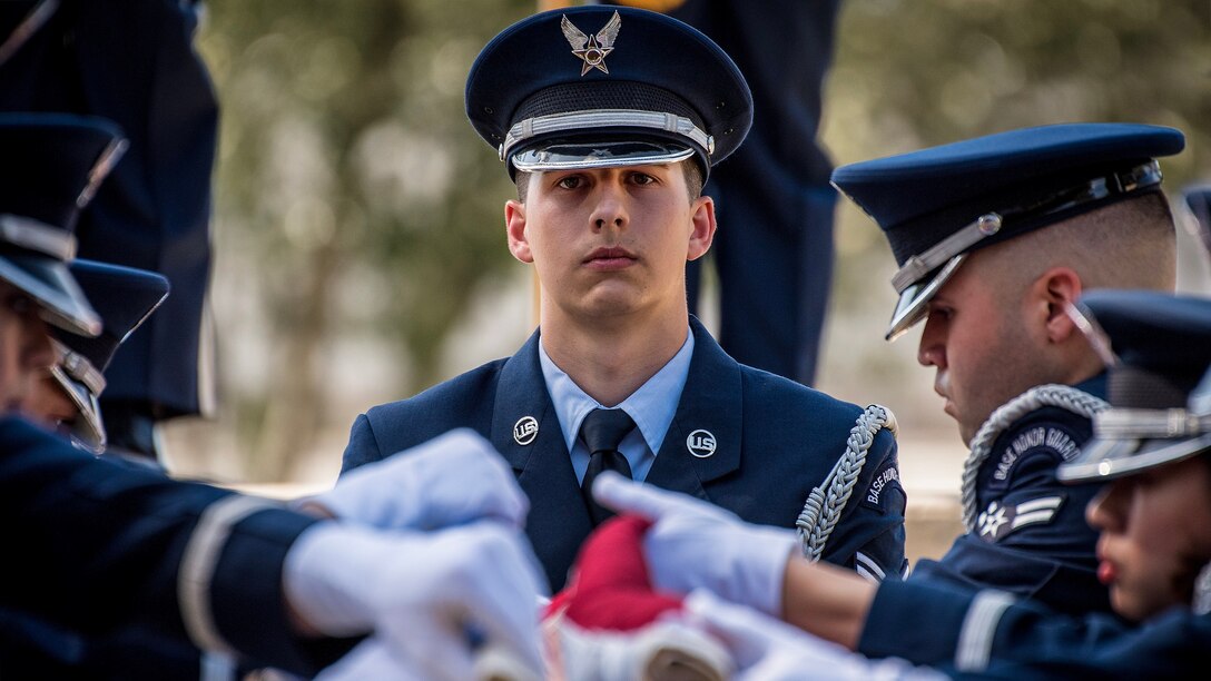 An airman watches as other airmen fold an American flag.