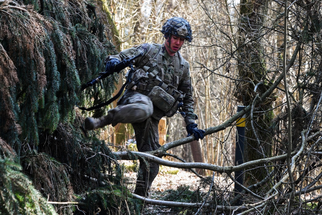 A soldier maneuvers through rugged terrain.