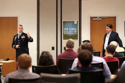 Army Reserve Col. Daniel Jaquint, left, G3 operations chief for the 85th Support Command, gives remarks about his civilian employer, Joe White, Senior Vice President of Enterprise Mobile Computing at a company quarterly meeting in Long Island, New York, Mar. 1, 2018.