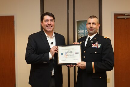 Joe White, Senior Vice President of Enterprise Mobile Computing, left, and Army Reserve Col. Daniel Jaquint, G3 operations chief for the 85th Support Command, pause for a photo after a surprise award presentation at a company quarterly meeting in Long Island, New York, Mar. 1, 2018.