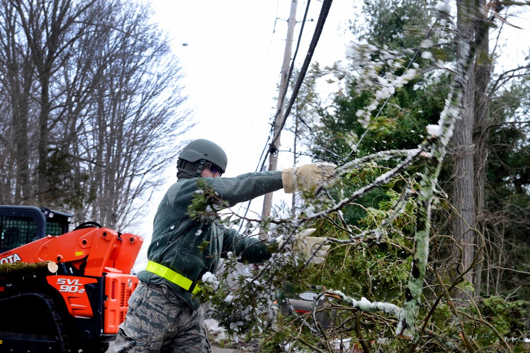 An airman removes branches and debris from a power line.