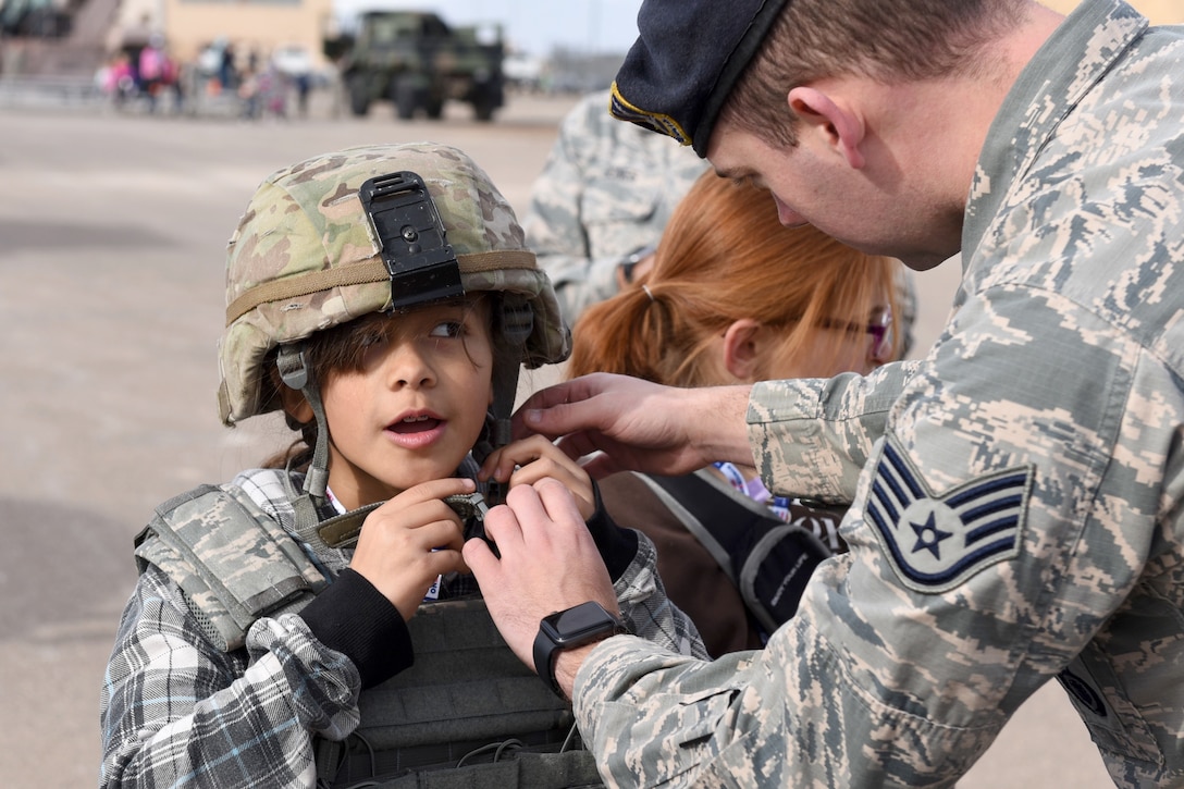 An airman helps a child put on a helmet.