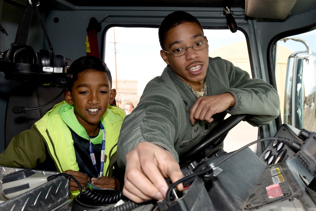 A child watches an airman turn a dial in a truck.
