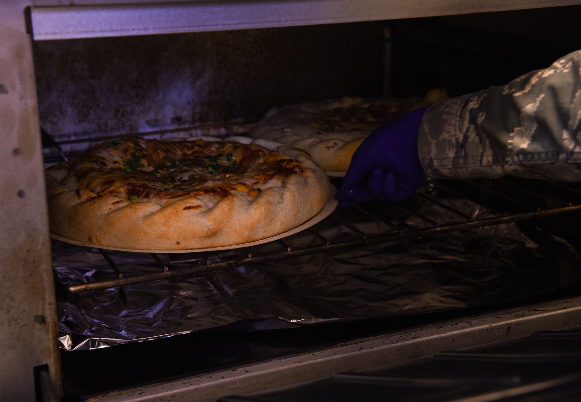 Airman 1st Class Kathleen Reynolds, 90th Force Support Squadron missile chef, places a pizza into the oven in preparation for lunch time at a missile alert facility, March 3, 2018, in the F.E. Warren Air Force Base missile complex. Missile chefs have a number of responsibilities in the field. While on location, they spend their days cooking, cleaning, and taking orders for anyone in the MAF. (U.S. Air Force Photo by Airman 1st Class Braydon Williams)