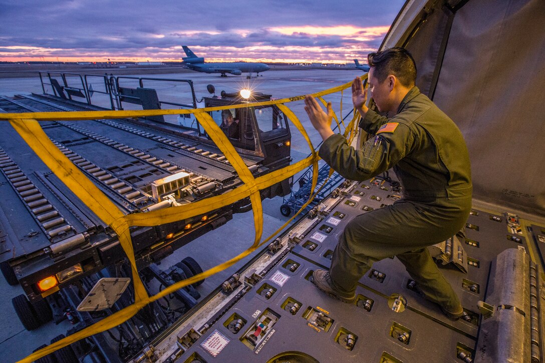 An airman uses his hands to signal the operator of an aircraft loadr/transporter.