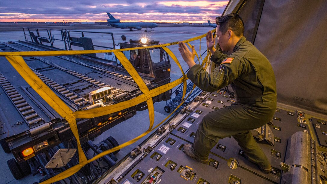 An airman uses his hands to signal the operator of an aircraft loadr/transporter.
