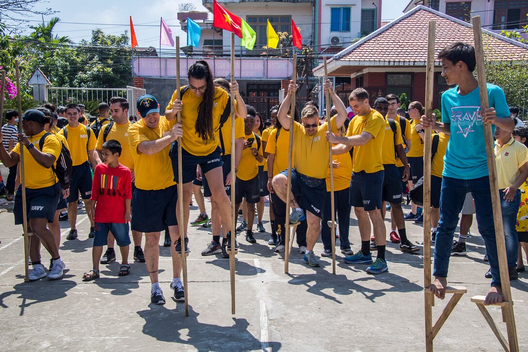 Sailors walk on stilts during a visit with children during a community event.